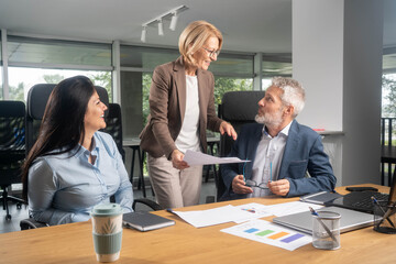 Three busy happy middle aged professional business man and two women executive leaders team using laptop working on computer at work desk having conversation on financial project at meeting in office.