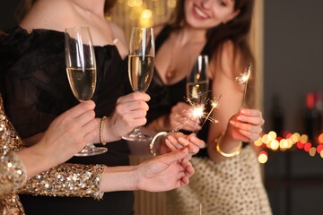 Women celebrating New Year with sparklers and wine glasses indoors, closeup