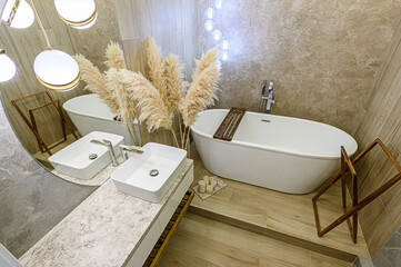 A stylish bathroom features a white bathtub, double sinks, pampas grass, and warm lighting. The...