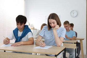Fototapeta premium Students taking exam at wooden table indoors