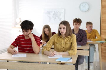 Students taking exam at wooden table indoors