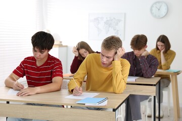 Students taking exam at wooden table indoors