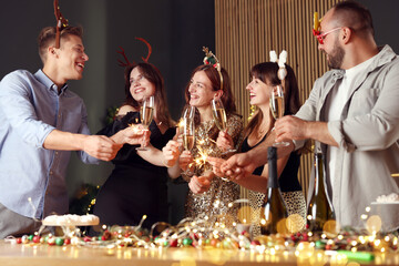 Friends celebrating New Year with sparklers and wine glasses indoors