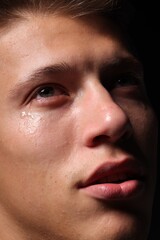 Obraz premium Sad man crying on black background, closeup