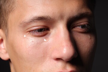 Sad man crying on black background, closeup