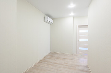 Bright, empty room with light wood flooring and white walls. An air conditioner is mounted high on one wall