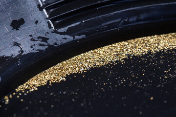Closeup view of gold flakes collected in a black panning pan. Shiny metallic particles representing mining, prospecting, natural resources, and the search for wealth and treasure.