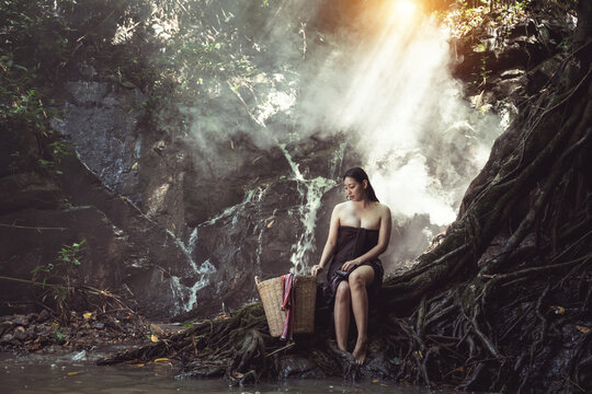 Serene Woman Sitting by Waterfall in Lush Forest, Embodying Peace and Nature's Beauty with Warm Light Filtering Through Trees - Powered by Adobe