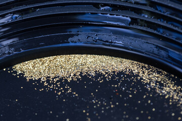 Closeup view of gold flakes collected in a black panning pan. Shiny metallic particles representing mining, prospecting, natural resources, and the search for wealth and treasure.