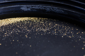 Closeup view of gold flakes collected in a black panning pan. Shiny metallic particles representing mining, prospecting, natural resources, and the search for wealth and treasure.