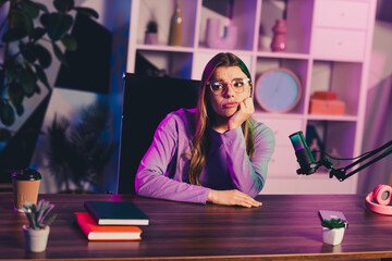 Video chat blogger in casual attire pondering ideas while sitting at a desk with microphone and office supplies