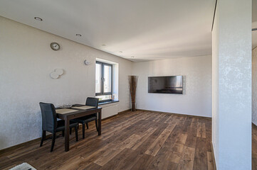 Fototapeta premium modern living and dining area featuring dark wood flooring, a dining table with chairs, a wall-mounted TV, and natural light from a window. The decor is minimalist and clean