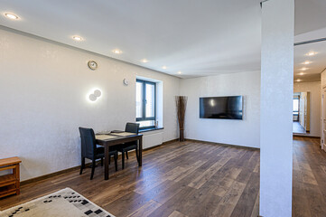Elegant living room with wooden floor, dining area, TV, and modern lighting. The color palette is primarily white and brown