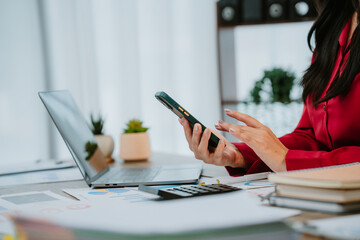 Fototapeta premium Smiling businesswoman talking on phone and holding tablet while working with documents and laptop in office