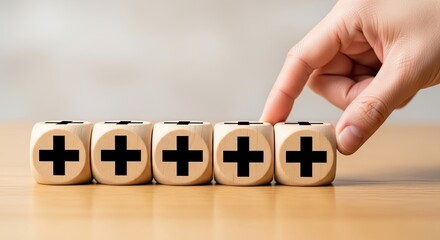 Fototapeta premium Hand Arranging Five Wood Dice Cubes Displaying Black Plus Signs on Light Brown Tabletop