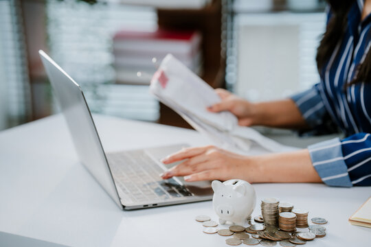 A person in business attire places a coin into a piggy bank beside a laptop, symbolizing saving money and financial management. - Powered by Adobe