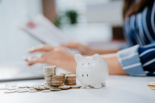 A person in business attire places a coin into a piggy bank beside a laptop, symbolizing saving money and financial management.