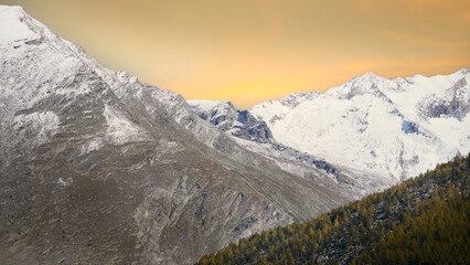 Majestic snow-capped mountains rise against a vibrant sunset sky, showcasing rugged terrain and lush green forests, creating a breathtaking natural landscape scene