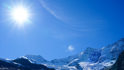 Majestic snow-capped mountains under a bright sun, showcasing a clear blue sky and stunning natural landscape, perfect for outdoor adventure and exploration themes