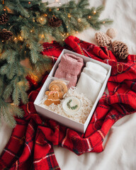 Cozy gift box featuring soft socks, a gingerbread cookie, and a candle, surrounded by festive greenery and a red plaid blanket, perfect for holiday gifting and seasonal warmth
