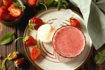 Fresh strawberry protein smoothie on a wooden table with fresh strawberries and a protein powder.