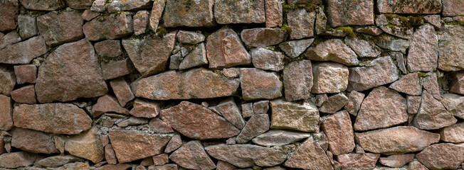 Rustic stone wall features various sizes and shapes of stones, some covered with moss, texture and background