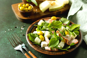 Fresh arugula salad with prosciutto, melon, and olives for a delicious summer meal. Copy space.