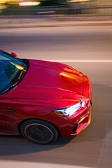 Sleek red sports car captures motion blur on a sunlit road at dusk