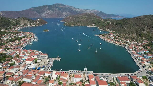 Drone aerial footage of Serene harbor of vathy city  on a Greek island of Ithaki surrounded by mountains and lush greenery. Sailboats float peacefully in the clear blue water under a bright sky.