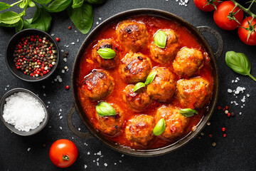 Meatballs in tomato sauce in iron plate on black background.