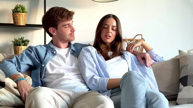 Happy couple sitting together on sofa at home, talking and laughing pleasantly, sharing confessions, gossip, work or daily life, symbol of love, friendship, happiness, positive relationship