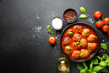 Meatballs in tomato sauce in iron plate on black background.