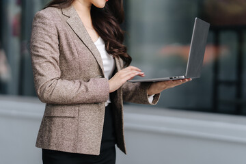 Modern Professional: A focused professional, elegantly dressed, engages with her laptop outdoors,...