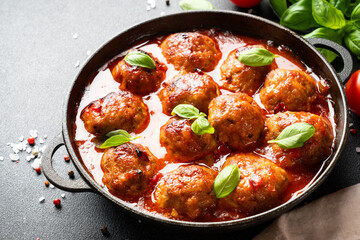 Meatballs in tomato sauce in iron plate on black background.