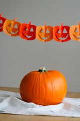 Minimal halloween decor with pumpkin on linen fabric and paper garland in background