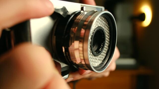 Photographer hands adjusting settings on classic vintage film camera, with lens aperture blades opening, closing in dimly lit warm environment. Photographer adjusting vintage film camera lens aperture