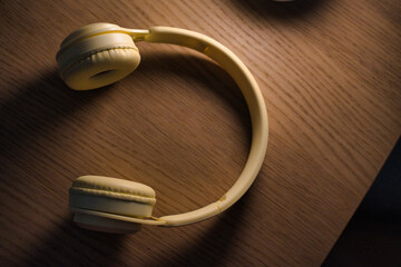 Yellow wireless headphones are lying open on a textured wooden table, representing concepts of relaxation, home entertainment, technology, and portable audio enjoyment