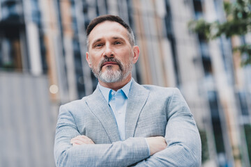 Naklejka premium Confident mature businessman in a modern city wearing a sharp suit standing in the urban streets conveying professionalism and success for a corporate real estate and office market photoshoot
