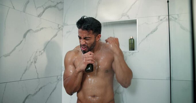 Man, shower and singing in home bathroom for cleaning, wellness and washing hair. Male person, house and running water in morning for karaoke, grooming splash and fresh body with cosmetics bottle