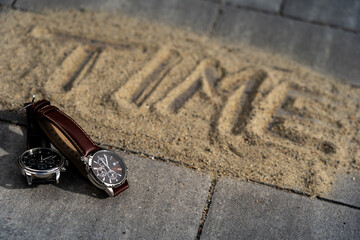 Two business quartz watches symbolize the changing of time. In the background, the word "TIME" written in the sand symbolizes the passage of time.