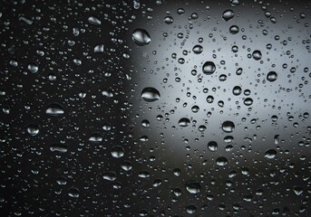Raindrops on a glass surface, conveying a sense of freshness and tranquility. The droplets are clear and round, reflecting light, with dark blurry background.