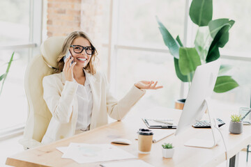 Confident businesswoman talking on smartphone at her desk surrounded by modern office interior plants and work elements