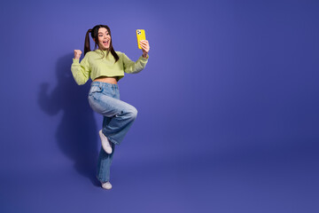 Cheerful young woman with a smartphone gesturing playfully against a vibrant purple backdrop in...