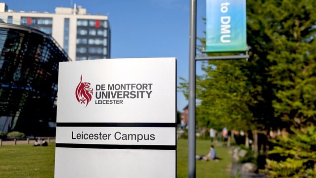 Leicester, England, UK - 14 May 2025: De Montfort University Leicester campus entrance sign with modern buildings and students relaxing on the grass