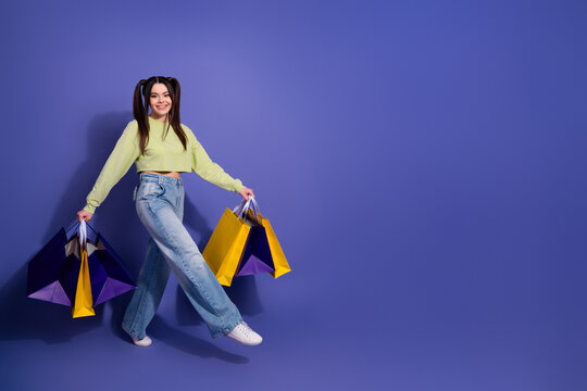 Young woman holding vibrant shopping bags against a purple background, showcasing joy and fashion with a charming smile