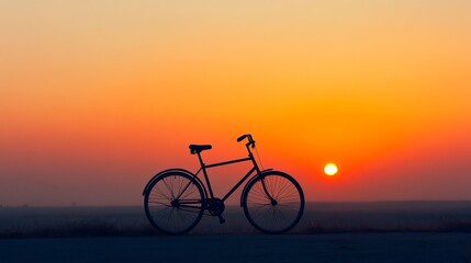 Obraz premium Dramatic silhouette of a bicycle against a vivid orange and yellow sunset sky, symbolizing freedom, adventure, and the end of a journey