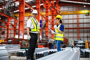 Smiling industrial worker woman talking with supervisor. Industrial workers with clipboard checking metal sheets and report with manufacturing process supervisor.