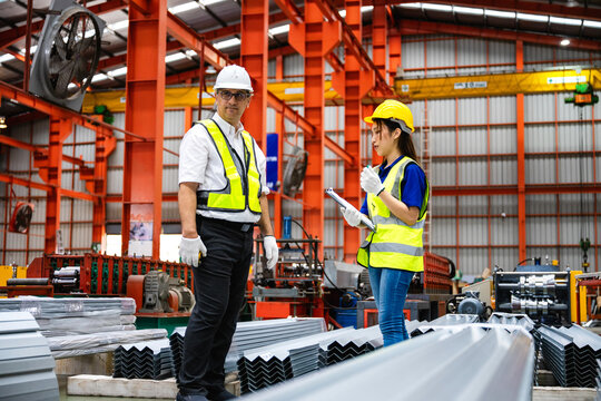 Smiling industrial worker woman talking with supervisor. Industrial workers with clipboard checking metal sheets and report with manufacturing process supervisor.