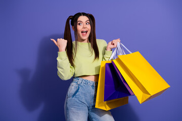 Excited young woman with shopping bags gesturing on violet background displaying joy and...