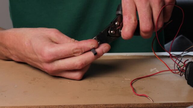 Man holding a heat shrink tube to cover electrical wires during a wiring repair process at a home electronics workspace